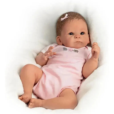Ashton Drake Little Peanut Baby Doll Girl wearing a pink onesie with elephant designs, posed on a soft white blanket.