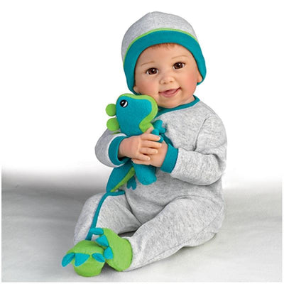 Ashton Drake Ryan And Rex Baby Boy Doll wearing a gray outfit with teal accents, holding a plush dinosaur toy.