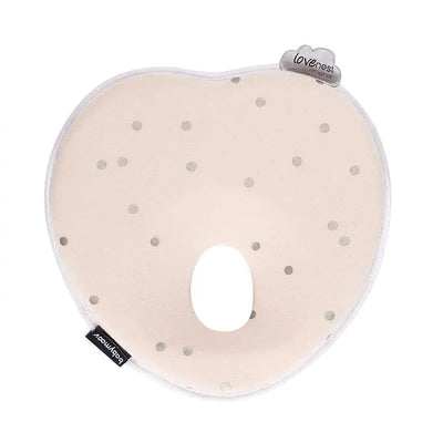 Heart-shaped baby pillow in soft pink with gray polka dots, featuring a central cutout and Babymoov branding.