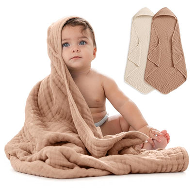 Hooded baby towels in cedar and sand colors, draped around a smiling baby sitting on the floor.