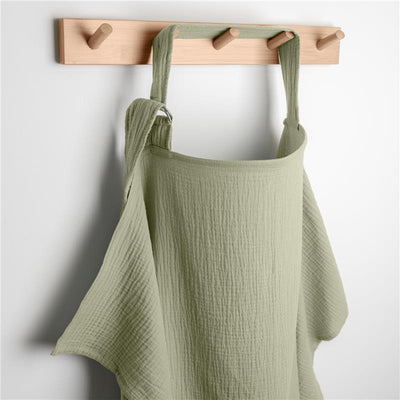 Muslin nursing cover in sage green, hanging on a wooden hook, designed for privacy while breastfeeding.