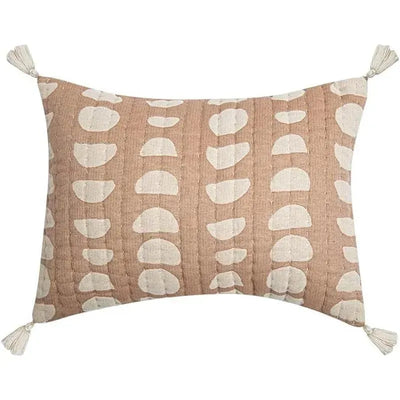 Copper moon phase pillow with a textured blush background, featuring white crescent shapes and decorative tassels on corners.