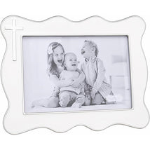 White enamel cross picture frame with a scalloped edge, holding a black and white photo of three smiling children.