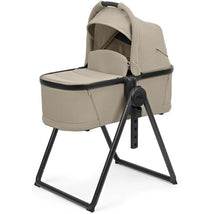 Peg Ypsi Bassinet in Vanilla Blend features a beige fabric with a sturdy black stand, designed for infants.