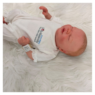 Reborn Doll White Vinyl Ever dressed in a white outfit, lying on a padded surface with a serene expression.