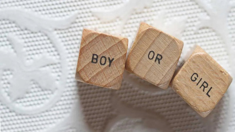 Wooden blocks spelling 'BOY OR GIRL' on textured white surface, baby gender reveal theme