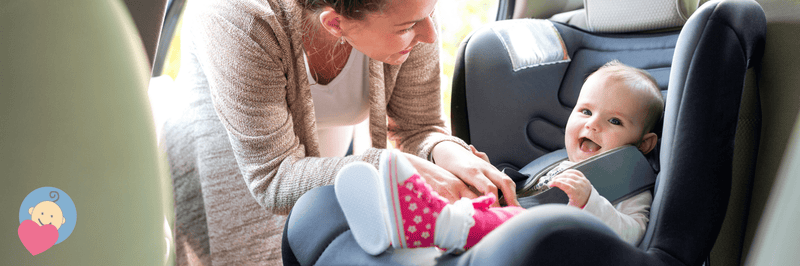 Mom securing baby in car seat, baby smiling happily in pink outfit