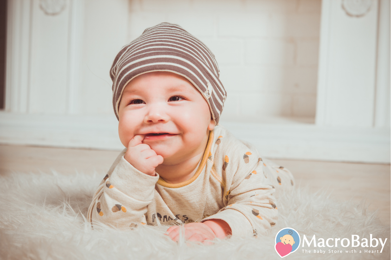 Smiling baby wearing striped hat and acorn print onesie on fluffy rug