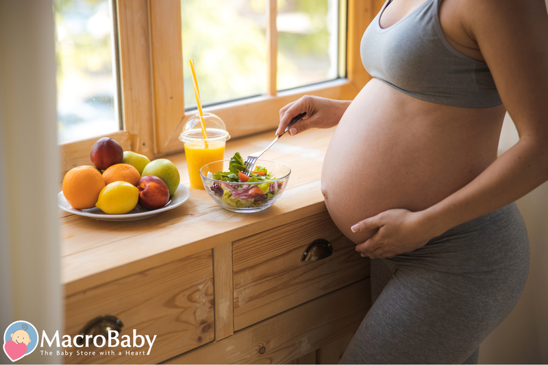Pregnant woman eating healthy salad and fruit by window, prenatal nutrition