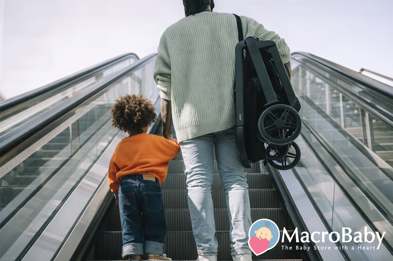 Parent carrying folded stroller up escalator with child, ideal for baby gear on the go
