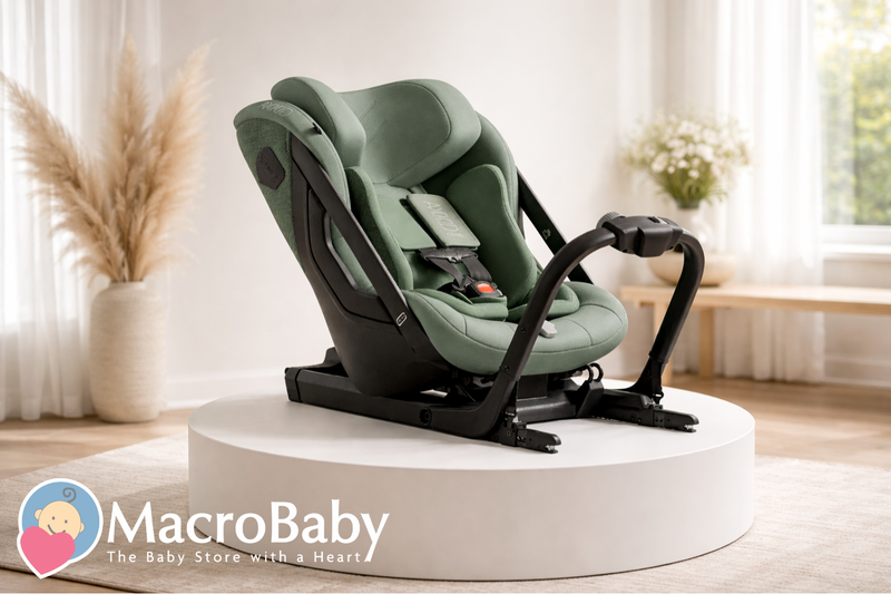 Green baby car seat with black base, displayed on white pedestal in bright room