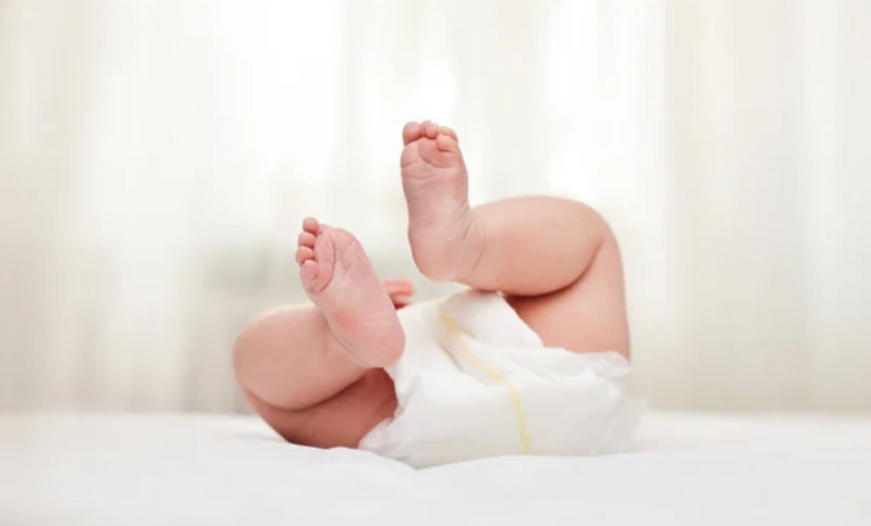 Baby's feet in diaper on soft bedding, perfect for newborn care and comfort