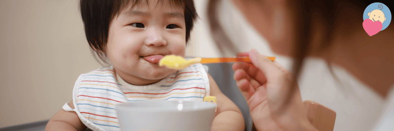 Happy baby eating puree with spoon, wearing striped bib, ideal for baby feeding essentials