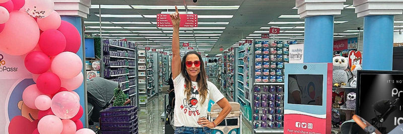 Woman in baby store aisle pointing at signage near pink balloon arch and strollers