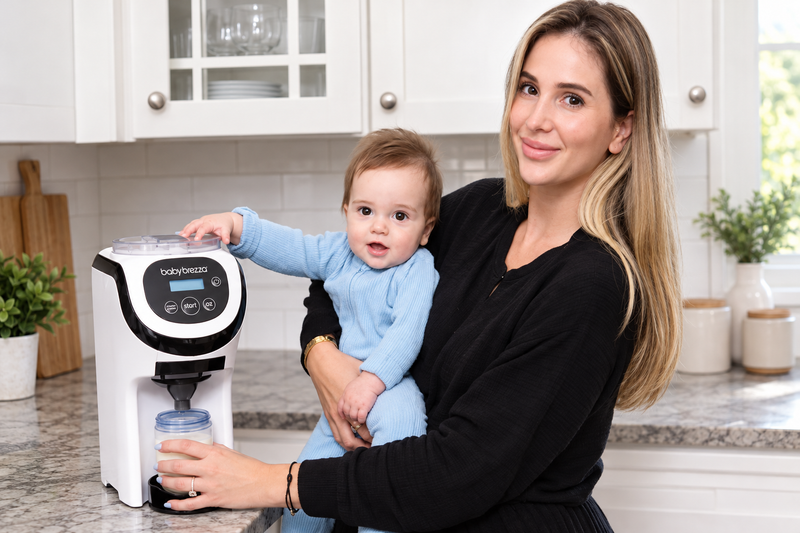 Mother holding her baby while preparing a bottle with a Baby Brezza formula dispenser.
