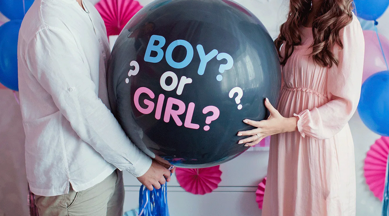 Couple holding gender reveal balloon with 'Boy or Girl?' text at baby shower party