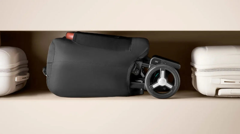 Compact black stroller with wheels stored on shelf beside white luggage