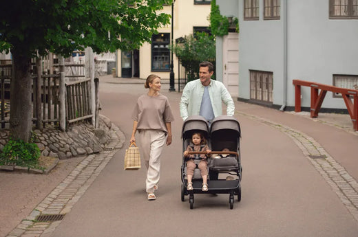 Parents walking with twin baby stroller on paved street, ideal for urban family outings and baby gear needs