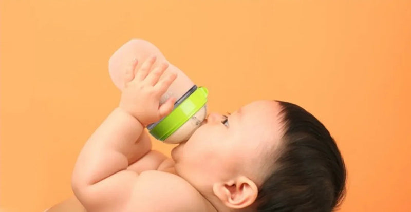 Baby drinking from green and clear baby bottle against orange background