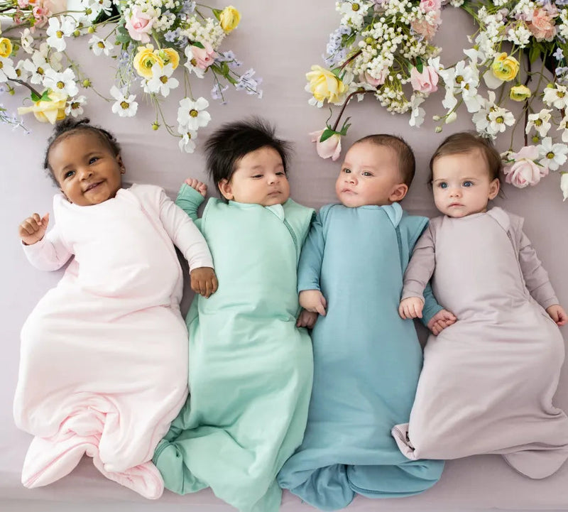 Four babies in colorful sleep sacks on floral backdrop, ideal for baby bedding and comfort