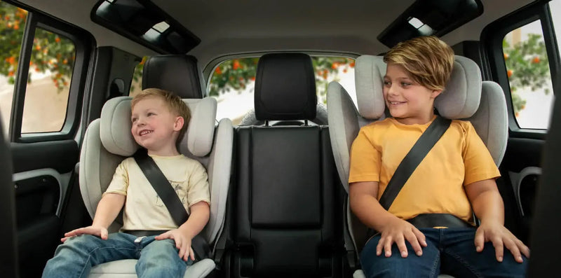 Two happy kids secured in car seats inside a vehicle, showcasing safe and comfortable baby car seat travel.