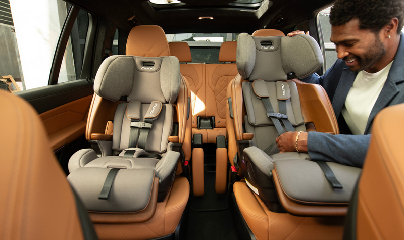 Man adjusting gray Nuna car seats in luxury SUV with tan leather interior
