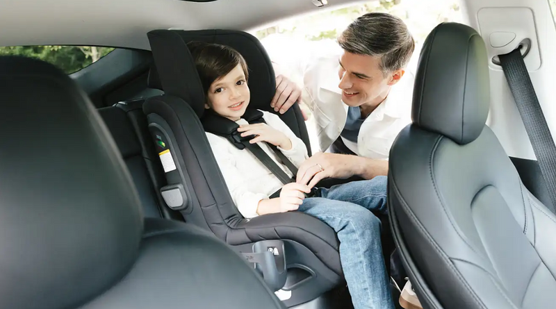 Dad securing child in black car seat inside vehicle, safe travel for kids