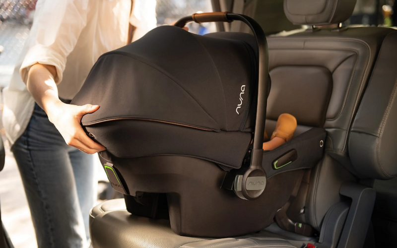 Nuna infant car seat with canopy, installed in car, mom adjusting cover