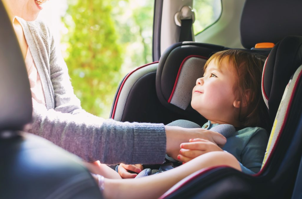 Toddler in car seat with mom adjusting harness, safe travel for babies
