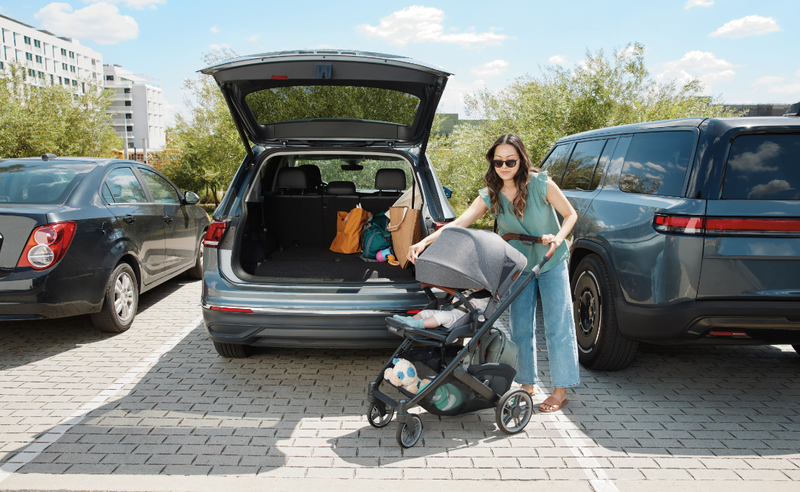 Mom with baby stroller beside open SUV trunk, ready for outing with baby gear and shopping bags
