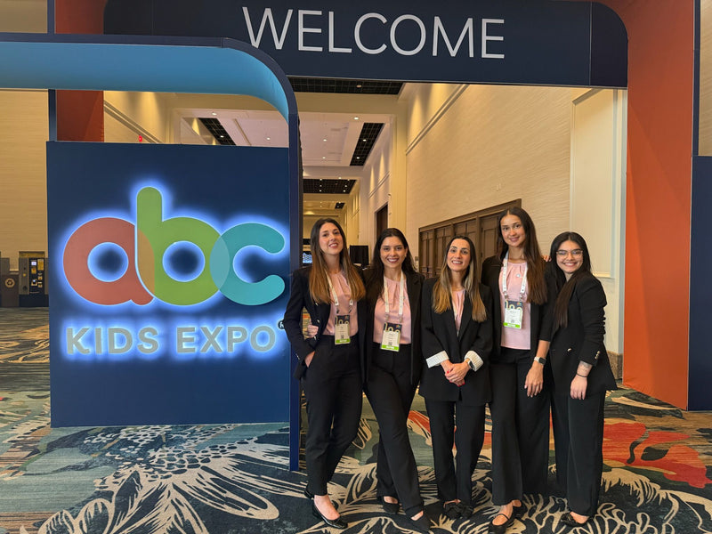 Five women in business attire pose at ABC Kids Expo entrance, showcasing baby and kids industry event