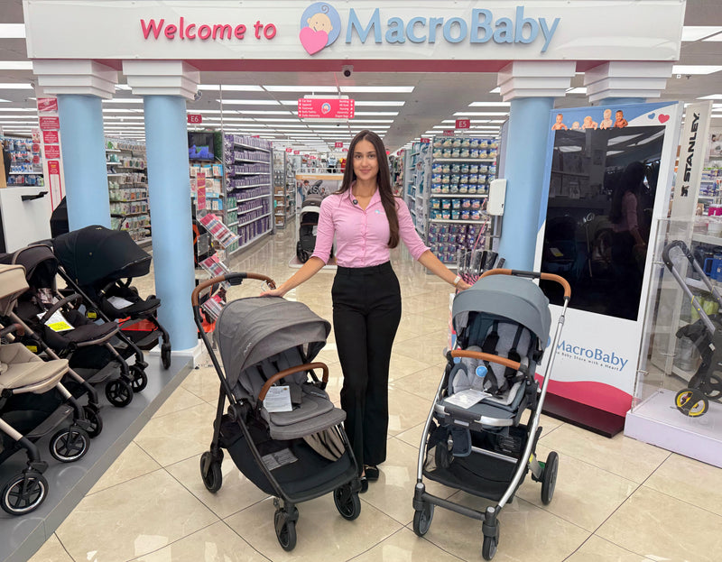 Woman showcasing baby strollers in a MacroBaby store aisle, featuring modern designs and comfortable seating for infants and toddlers.