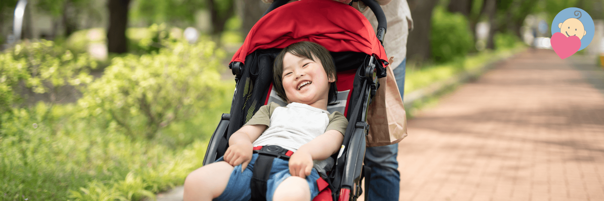Happy toddler smiling in red stroller on park path, enjoying outdoor baby gear