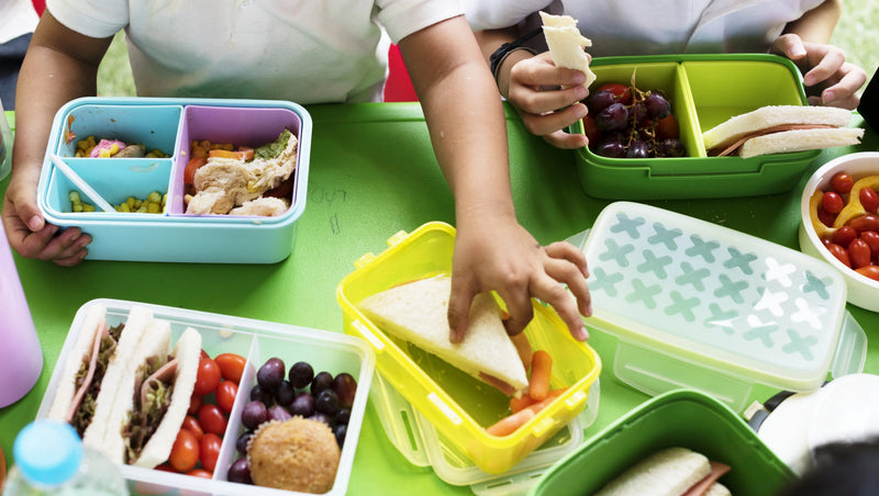 Kids enjoying colorful bento boxes with sandwiches, grapes, and veggies for healthy school lunches.