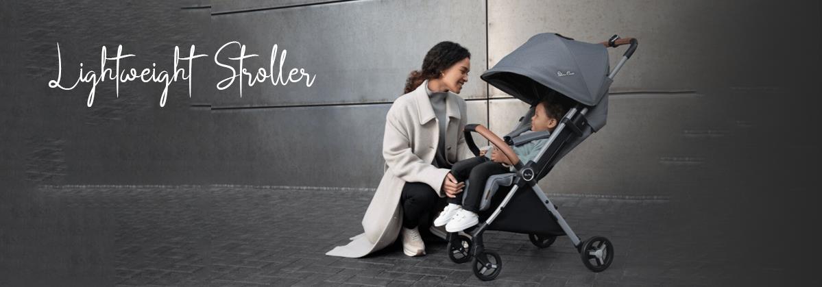 Mom kneeling beside child in gray lightweight stroller on city sidewalk