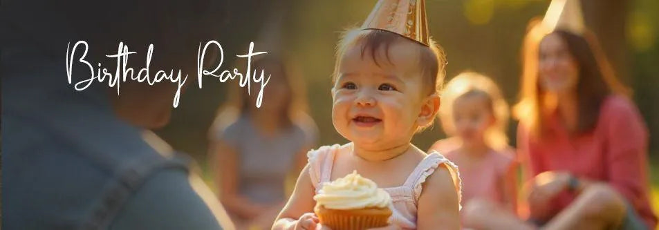Happy baby in party hat holding cupcake at outdoor birthday party with family