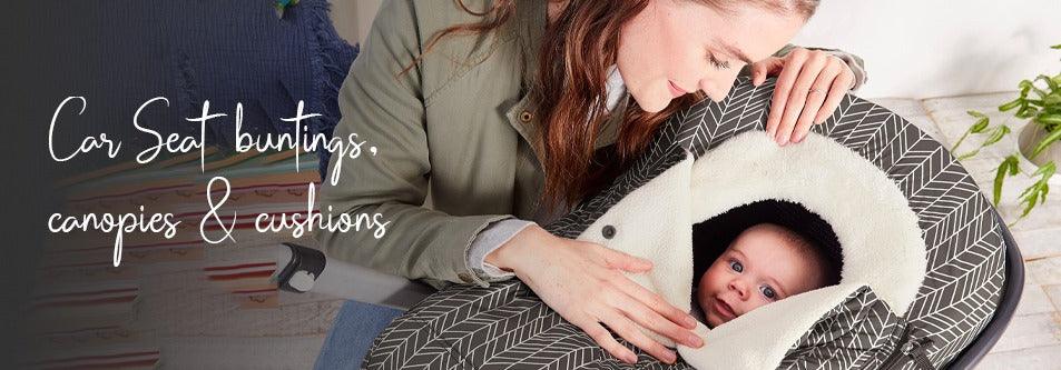 Baby in car seat with cozy canopy and cushion, mom gently touching baby
