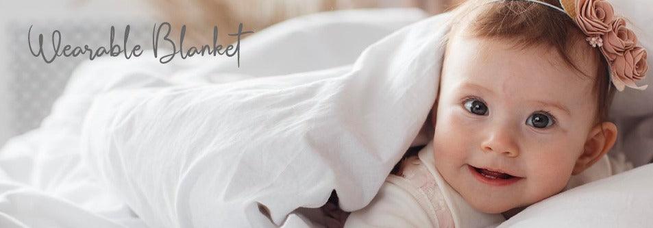 Baby wrapped in a wearable blanket, smiling with a flower headband
