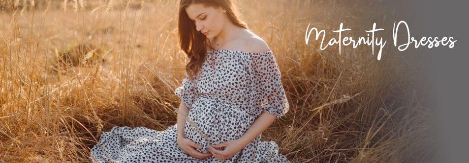 Pregnant woman in floral maternity dress, sitting in golden field, hands on belly