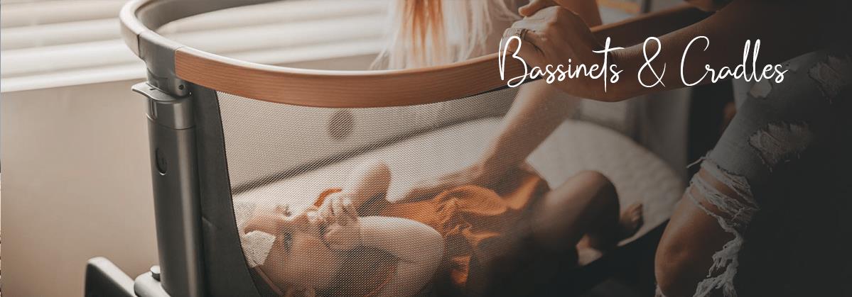 Baby sleeping in modern bassinet with mesh sides, mom gently touching baby, cozy nursery setting