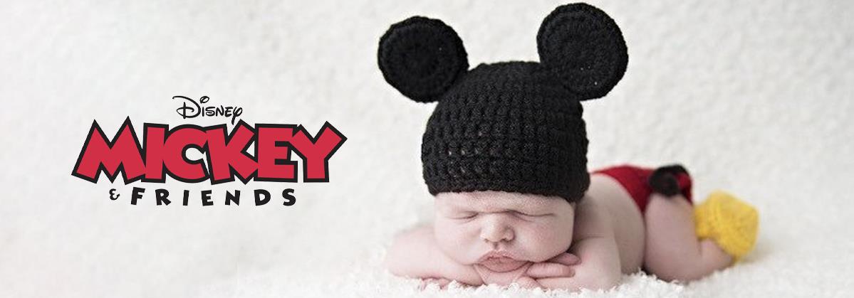 Adorable newborn baby wearing Mickey Mouse ears hat, red diaper cover, and yellow booties on white blanket