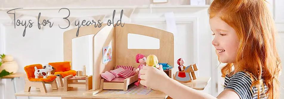 Toddler girl playing with wooden dollhouse toys for 3 year olds, featuring furniture and dolls.