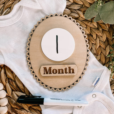 Baby onesie with wooden 1 Month milestone marker on woven mat