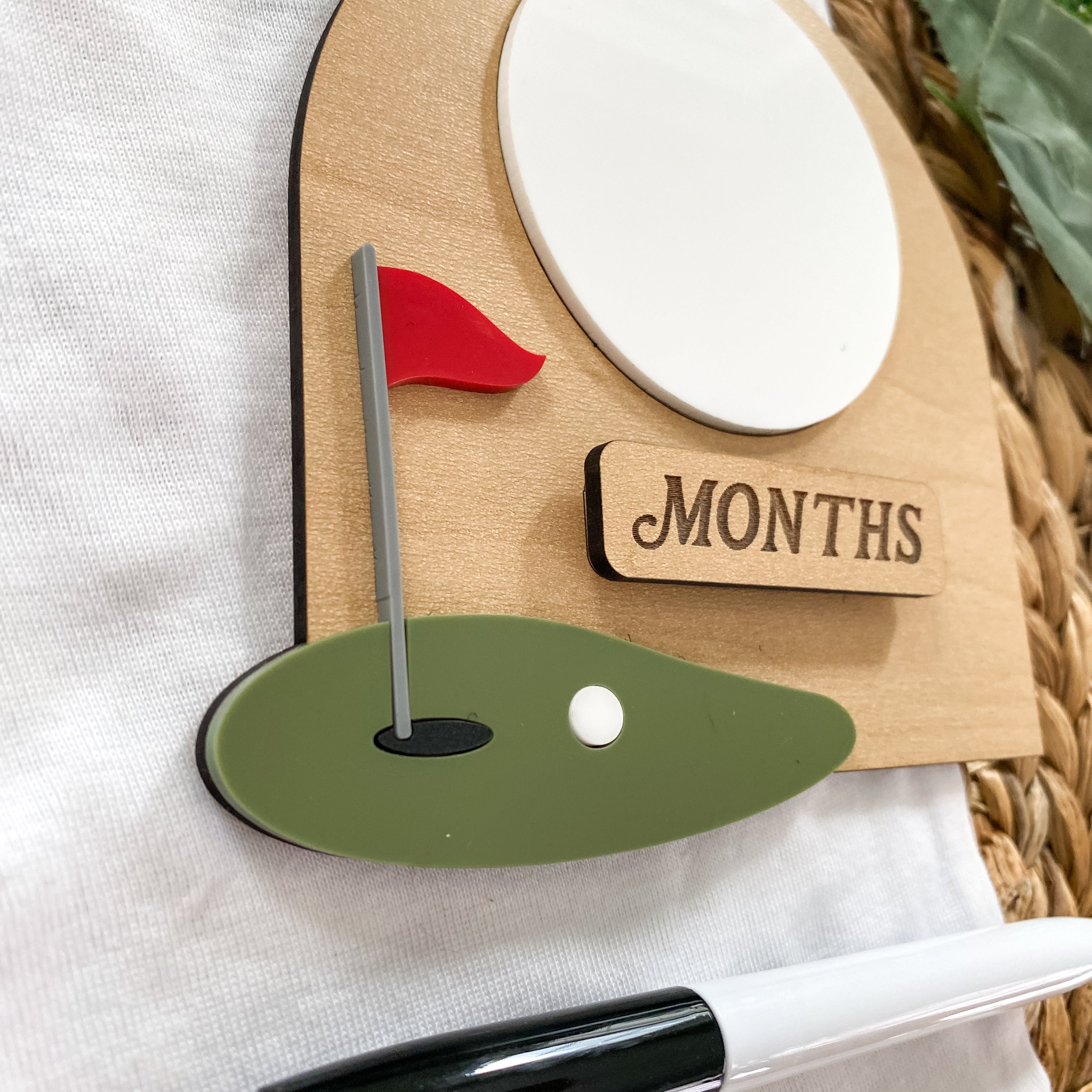 Golf-themed baby milestone tracker with red flag and 'MONTHS' label for baby development