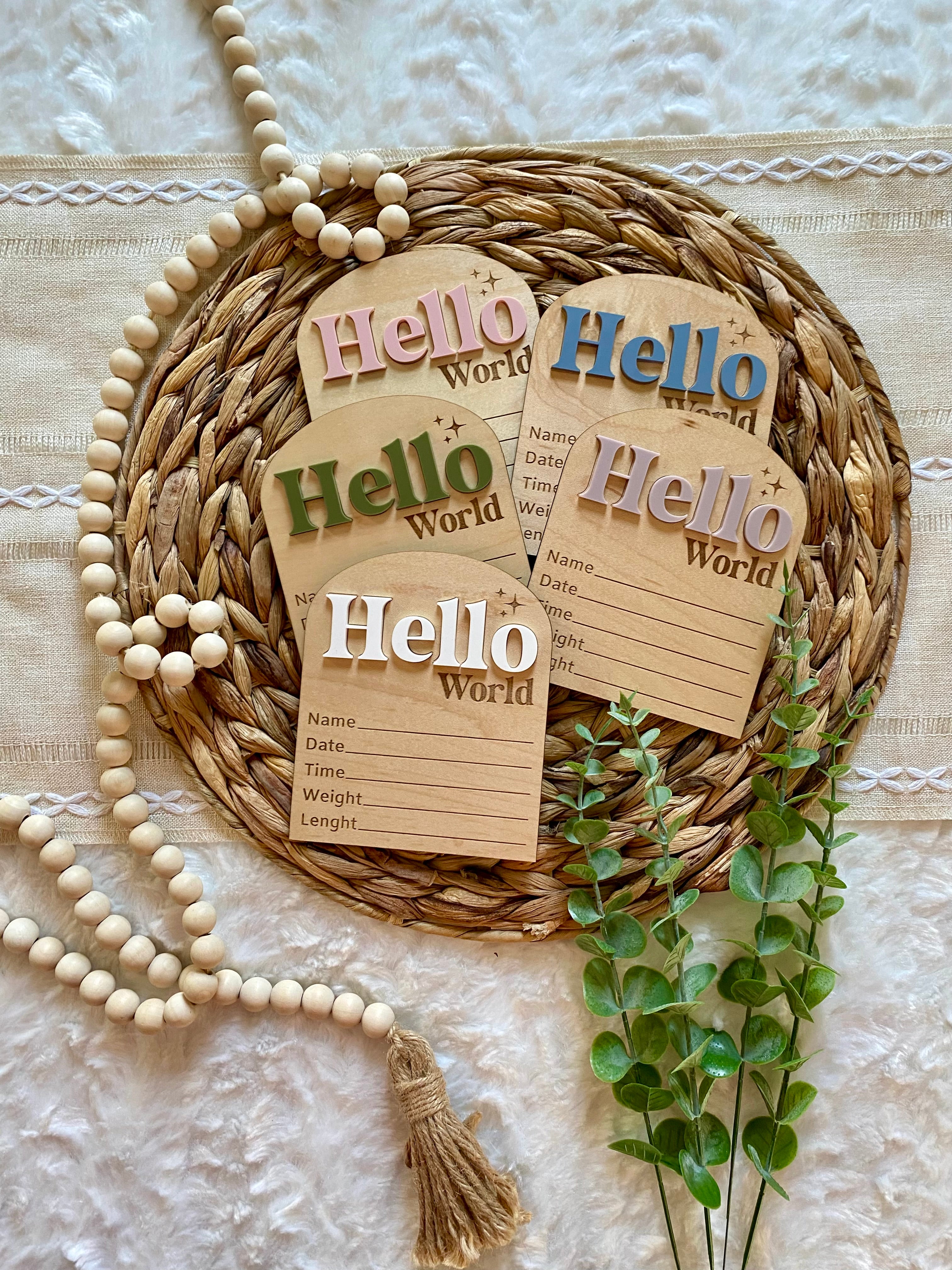 Hello World baby milestone cards with wooden beads and greenery on woven mat
