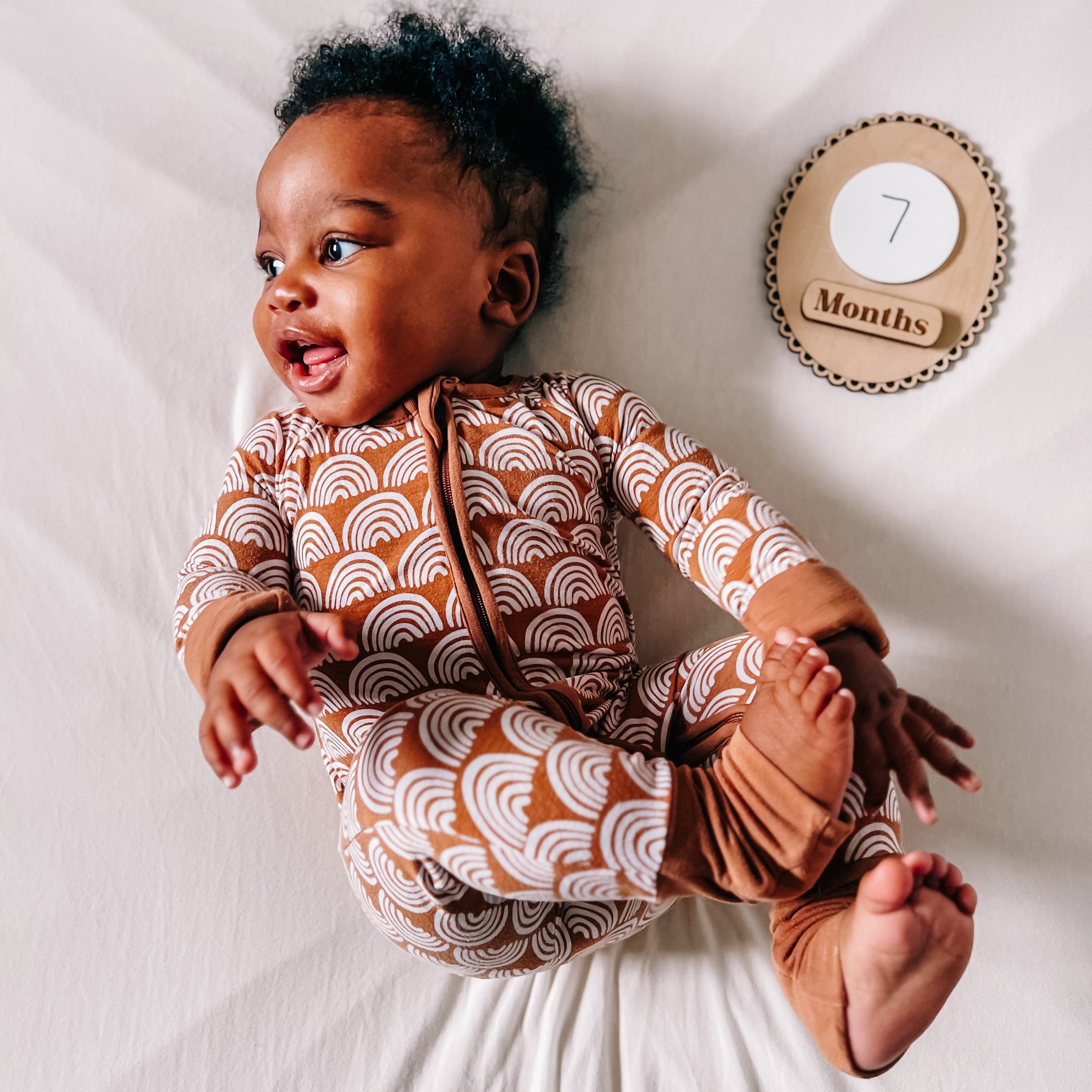 Baby in brown patterned onesie with 7 months milestone sign