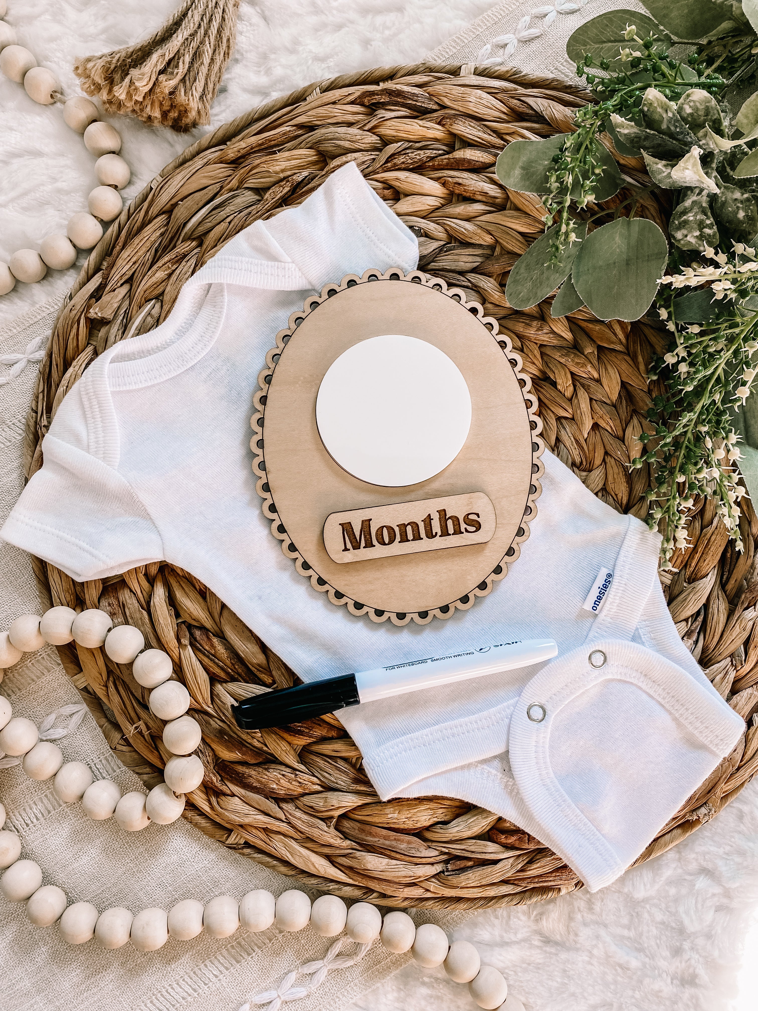 White baby onesie with wooden months milestone plaque on woven basket, ideal for baby photo props