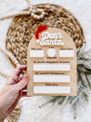 Wooden 'Dear Santa' letter template with fill-in blanks for kids' Christmas wishes and festive red hat accent.