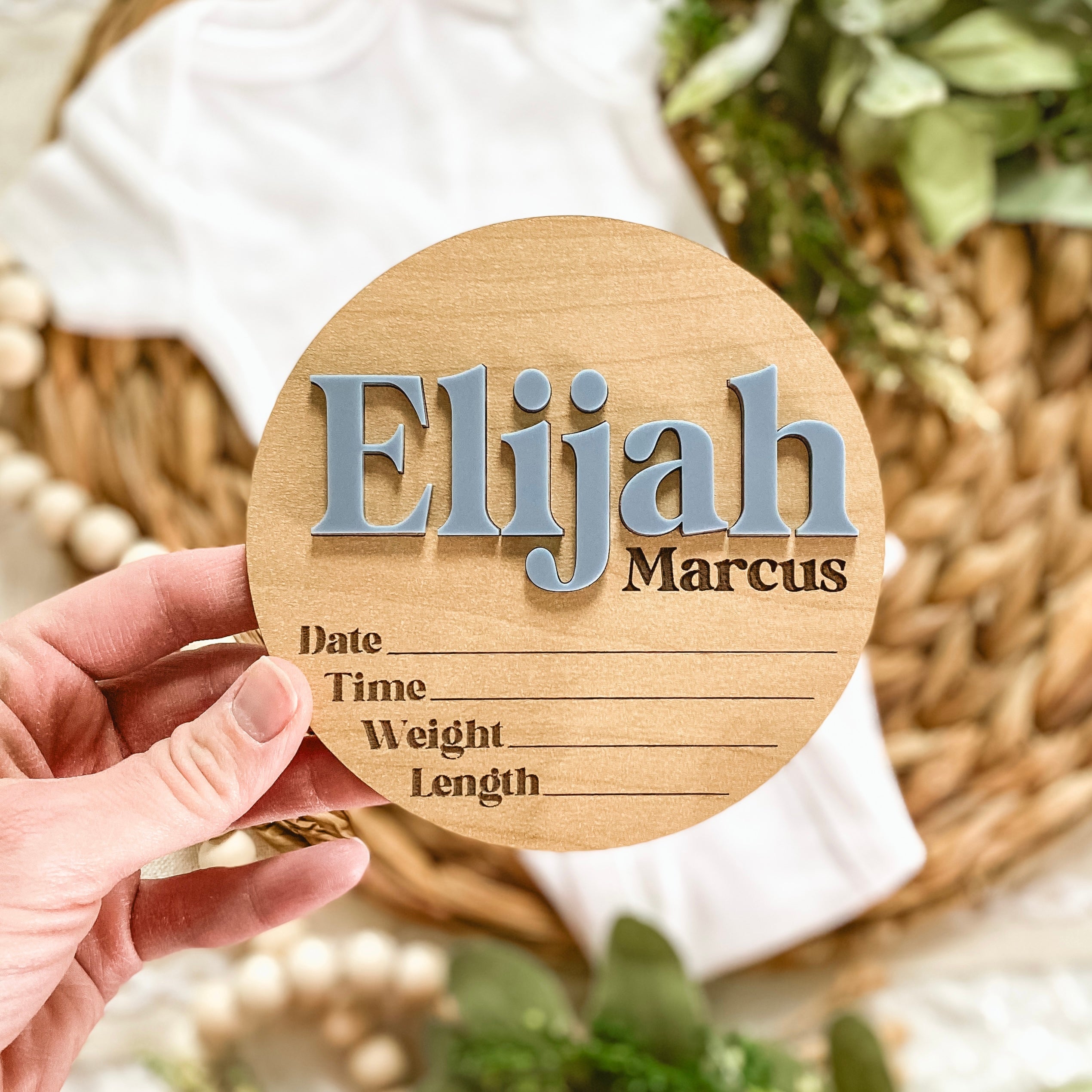 Personalized wooden baby name sign with Elijah Marcus, birth details, held over nursery basket