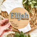 Personalized wooden baby name sign with Elijah Marcus, birth details, held over nursery basket